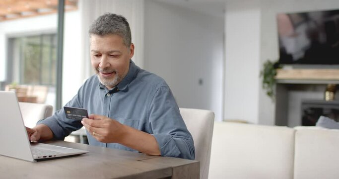 Happy senior biracial man using credit card and laptop online, copy space, slow motion