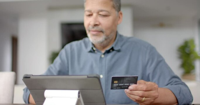 Happy senior biracial man using credit card and tablet for online payment, slow motion