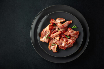  Roasted bacon slices with rosemary on a black plate.