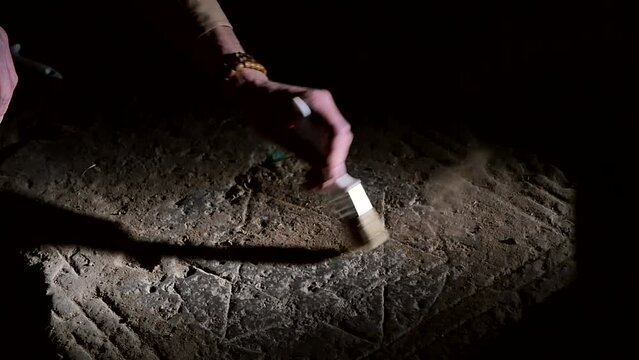 The hand of a male archaeologist holding a tool brush sweeps away dust and dirt on an ancient image of a six-pointed hexagram carved on a stone slab. Historical Jewish sign Star of David
