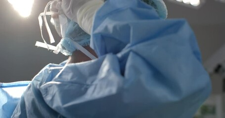 African american female surgeon wearing face mask in operating theatre, slow motion - Powered by Adobe