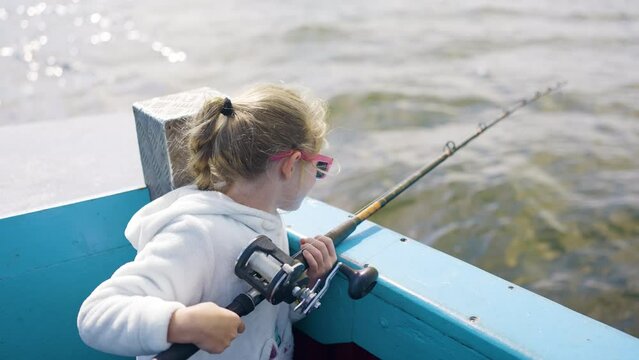 Young Girl Fishing Off Side Of A Blue Boat Sun Shining