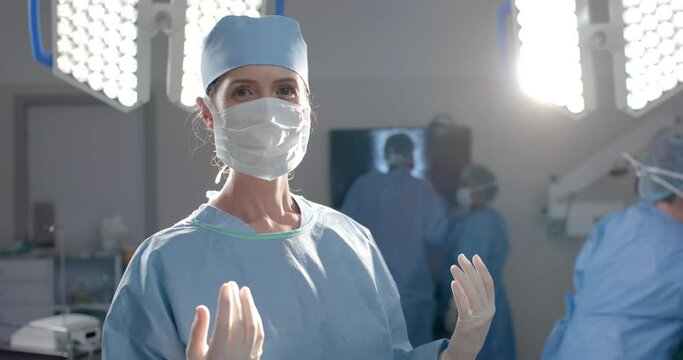 Portrait of caucasian female surgeon wearing surgical gown in operating theatre, slow motion