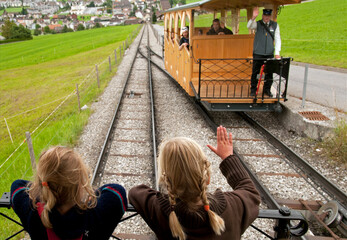 Stans, Nidwalden, Switzerland, Europe - funicular operator waves to two little girls, wooden retro train connects Stans town with change station leading to the top of Stanserhorn - obrazy, fototapety, plakaty