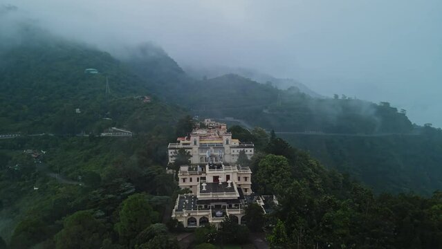 Aerial view of Narendra nagar Fort surrounded by green mountains during monsoon.Drone flying above the fort through green forest.
