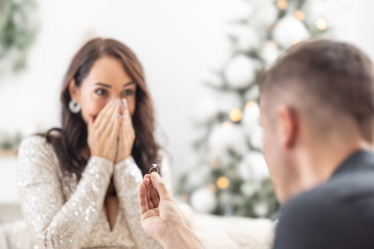 Christmas proposal by a man holding a ring in front of his surprised girlfriend