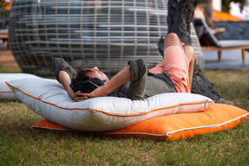Man lying on orange and white garden cushions in a luxury hotel garden.