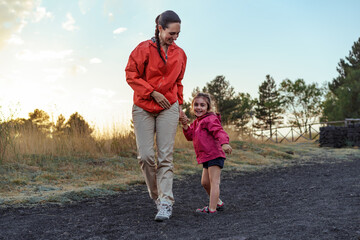 Fototapeta premium Mother and daughter holding hands and smiling during a leisurely walk, enjoying a beautiful outdoor setting together.