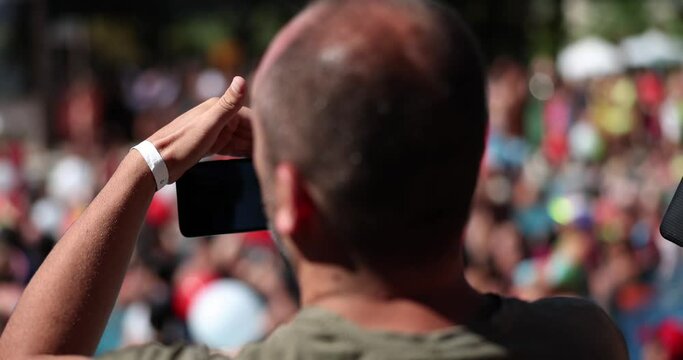 Man lifted his cell phone camera to film rally crowd of people or rear view concert. Filming sports competitions