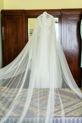 Elegant wedding dress hanging in the wardrobe, soft light caresses the white fabric, promises of a...