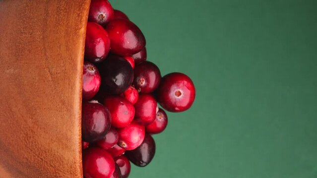 fresh red cranberries, rotation in circle. lingonberry red berries in a wooden bowl on a green background, Turning. selective focus. Vertical video