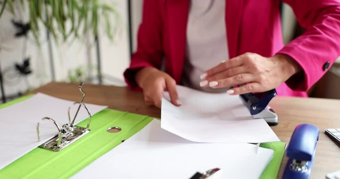 Secretary works in office and uses paper puncher. Documentation archive in folders