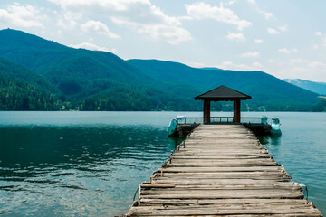 pier on the shore of the lake. pier with gazebo and fence, beautiful hills and mountains in the background. fishing and boating concept