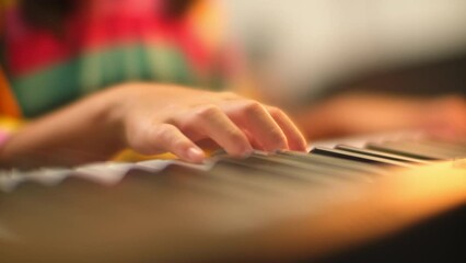 Close-up of a little student's hand playing the piano. Happy young Asian girl learning and practicing the piano. Selective focus.