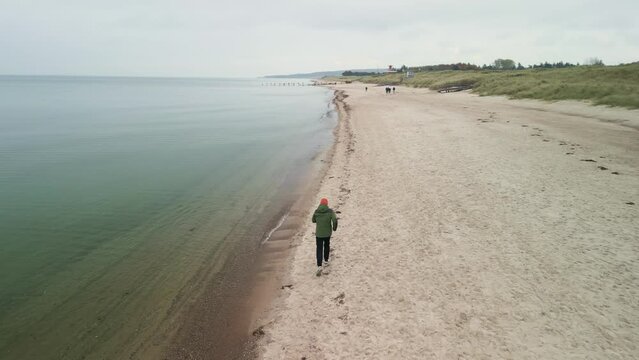 Ein junger Mann rennt an einem bew&ouml;lkten Tag am Strand entlang. Ein Mann l&auml;uft am Sand entlang.