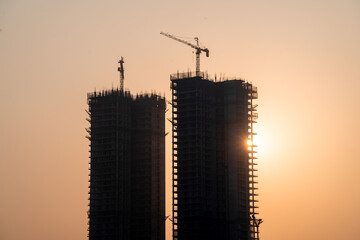 Silhouette of under construction building against sunset with crane on roof showing rapid real...