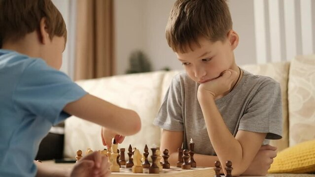 Two Caucasian boys are playing chess at home in living room. Older brother teaches younger one to play chess. Leisure game.