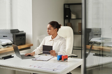 Young specialist of visa center concentrating on her online work on laptop while working with...