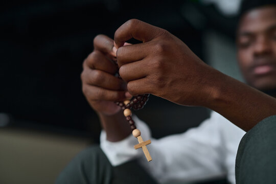 Close-up of African American man sitting with rosary beads and praying in difficult situation