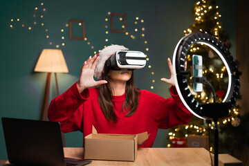 blogging, technology and people - happy smiling girl blogger in santa hat with ring light and smartphone doing VR glasses test live. concept of advertising products to bloggers on Christmas Eve