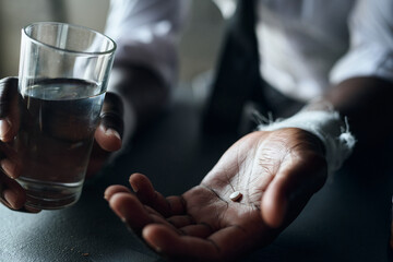 Close-up of African American young man taking painkiller pills with water