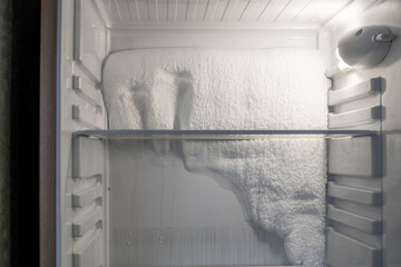 Frozen refrigerator that needs to be defrosted. Block of ice in the empty fridge. empty shelves in the refrigerator. Refrigerator maintenance.  - obrazy, fototapety, plakaty