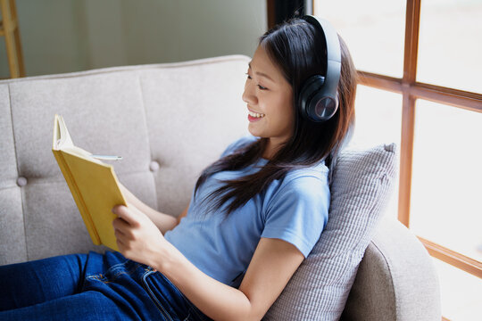 woman wearing headphones to listen music and reading notebook on sofa.