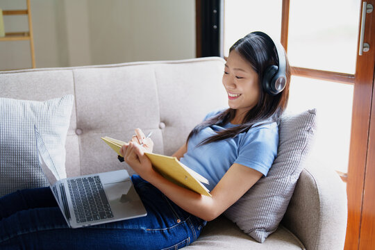 woman wearing headphones to listen music and reading notebook on sofa.