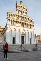 Fototapeta na wymiar A young Caucasian woman in front of San Michele in Foro, a Roman Catholic basilica located in Lucca, Tuscany, Italy. The church is built in Romanesque style and is located in the historic center.