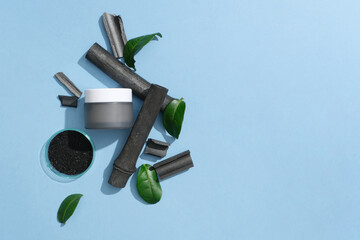 Bamboo charcoal powder is contained in a petri dish, a jar of unlabeled lotion, bamboo charcoal and green tea leaves are displayed on a blue background. Empty space for text design.