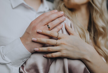 Hands with gold rings on the fingers of an embracing man and woman, bride and groom at a wedding. Photography, close-up portrait. - obrazy, fototapety, plakaty