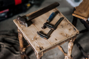 Metalworking metal tools, a hammer and a clamp lie on a wooden chair in the workshop. Close-up photography, industry concept.