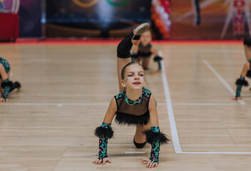 A stylish beautiful girl athlete in a cat, leopard costume, an 8-year-old child with makeup, face painting, dances, doing gymnastic exercises in the gym at competitions. Photography, sport concept.
