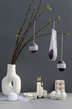 Studio shot of candles burning under laced Easter eggs hanging from twigs in vase