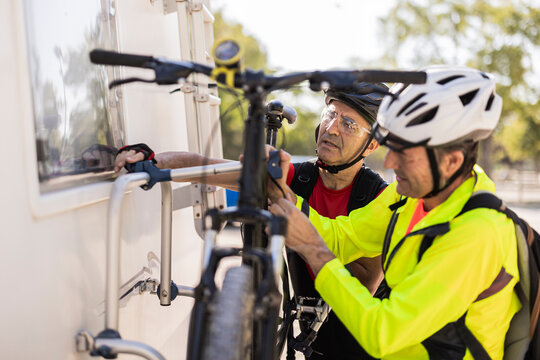 Friends wearing helmet and adjusting bicycle behind van