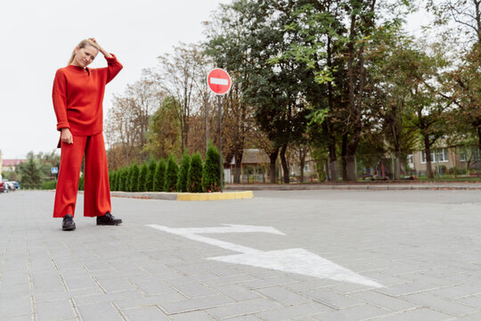Thoughtful woman with hand in hair standing near arrow sign on road