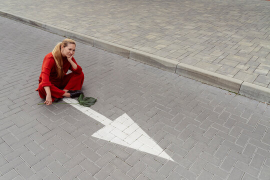 Contemplative woman with monstera leaf sitting near arrow sign on road