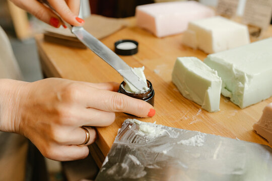 Hand of owner putting moisturizer in container on table in shop