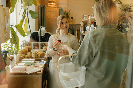 Smiling saleswoman selling moisturizer to customer in shop