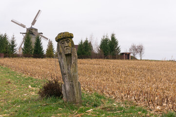 Sculpture carved from the trunk of a tree in a field. Old wooden mill.