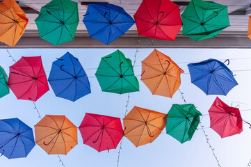 Sky is decorated with colorful umbrellas and lights. Broken multicolored umbrellas hanging between buildings.