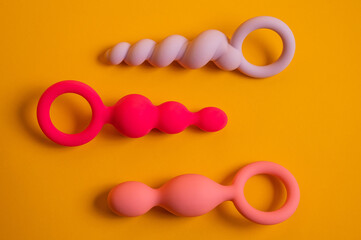 A set of three silicone anal beads of various shapes and sizes on an orange background.