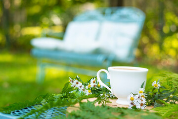 A cup of tea or coffee on a table in the garden and a cozy sofa with pillows in the background....