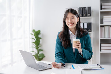 Fototapeta na wymiar Successful Asian businesswoman working and holding coffee cup at office. Confident Asia businesswoman sitting happily in the office.