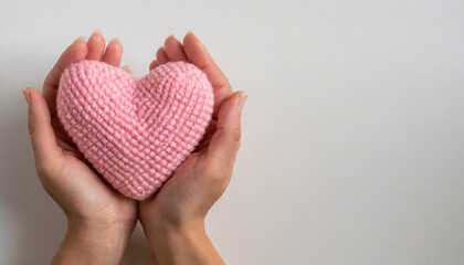 Female hands holding a pink heart knitted on a white background with copy space on a side