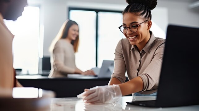 smiling bi-racial woman cleaning office desk with rag near colleague on blurred background.