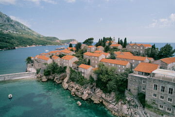 Fototapeta na wymiar Ancient buildings with red roofs behind the fortress walls on the rocky island of Sveti Stefan. Montenegro. Top view