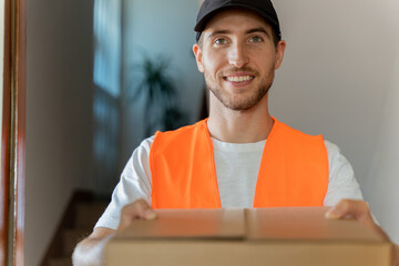Close-up of an attractive delivery man with cardboard box in his hands. Home delivery of packages - obrazy, fototapety, plakaty