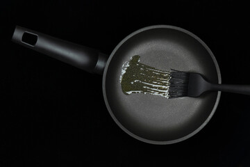 Black greasing silicone brush smears oil on frying pan. Concept for cooking, kitchenware...