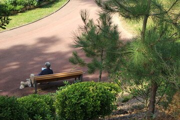 Une dame assise sur un banc avec son petit chien au parc des Dryades à La Baule